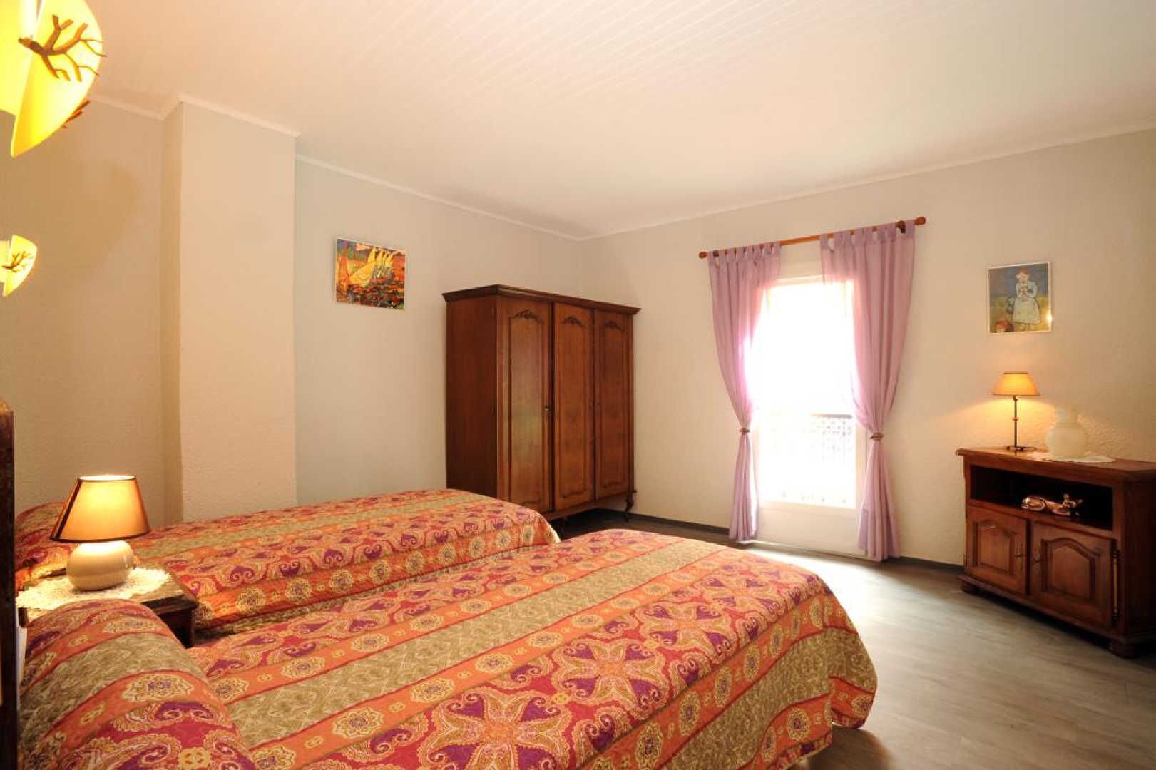 Une chambre avec deux lits, une armoire en bois, une table de chevet et une fenêtre avec des rideaux.