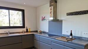 A modern kitchen with a large window, a built-in stove, and a wine bottle on the counter. - Eucalyptus - THUIR - Gîte (THUIR)