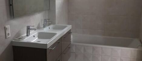 A modern bathroom with a double sink vanity, a large mirror, and a bathtub.