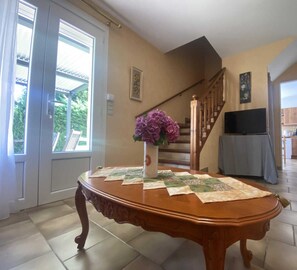 Un comedor con una mesa de madera, un jarrón de flores y una escalera que lleva a una cocina.