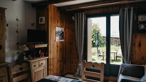 Une pièce chaleureuse aux murs en bois, avec un téléviseur posé sur un meuble en bois, une table recouverte d’une courtepointe et une vue sur l’extérieur grâce à une grande fenêtre.