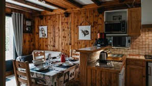 Une cuisine chaleureuse, aménagée dans le style d’un chalet, avec des murs en bois, un coin repas avec une table dressée pour deux personnes et un four à micro-ondes.