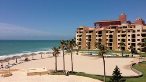 Un hotel frente a la playa con piscina, sombrillas y palmeras.