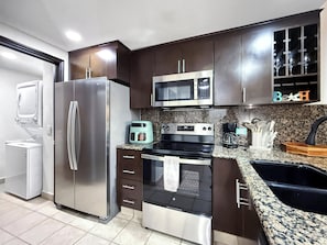 Una cocina moderna con electrodomésticos de acero inoxidable, armarios de madera oscura, encimera de granito y un vinatero empotrado.
