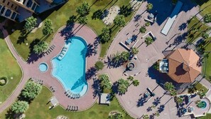 Eine Luftaufnahme eines Resorts mit einem zentralen Schwimmbad, mehreren Liegebereichen und Palmen.