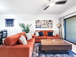 Una sala de estar moderna con dos sofás naranjas, una mesa de centro de madera, una planta grande y una pared decorada con motivos florales.