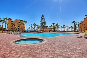 Zona de piscina de un complejo turístico con un jacuzzi circular, palmeras y vista al océano.