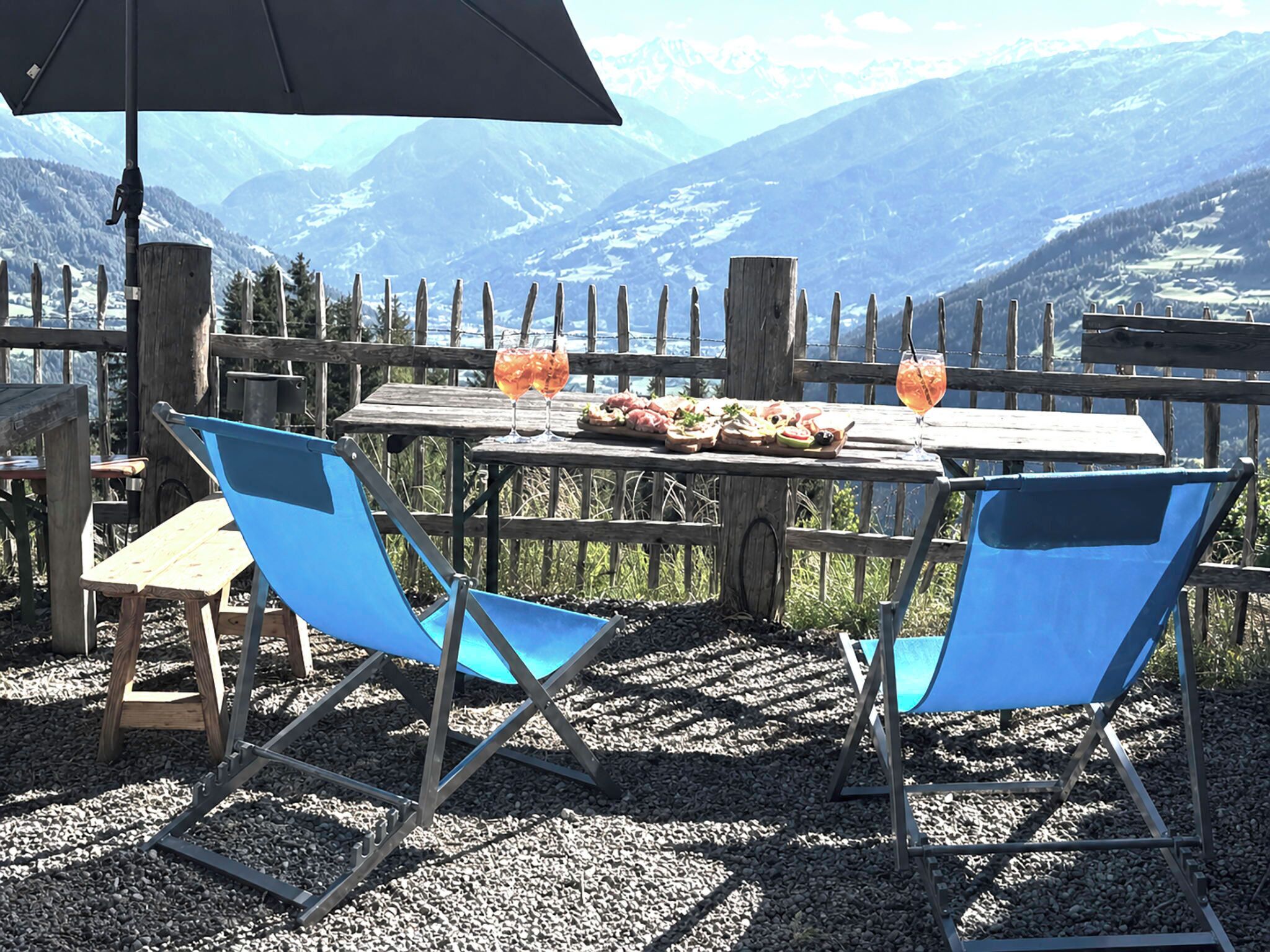 Une table en bois, deux chaises bleues, un parapluie noir et un verre contenant une boisson.
