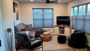 A living room with a sofa, armchair, coffee table, and a TV on a stand. - New charming bungalow with vast mountain views, easy access, stunning sunsets! (Waynesville)