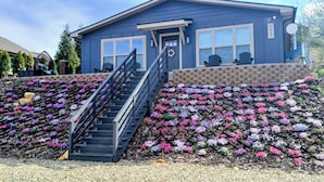 A house with a staircase leading to a porch, surrounded by a garden with purple and pink flowers. - New charming bungalow with vast mountain views, easy access, stunning sunsets! (Waynesville)