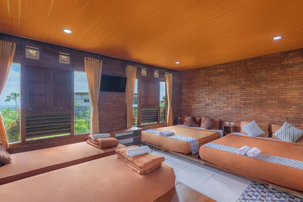 Habitación con dos camas, televisión y ventanas amplias con cortinas.