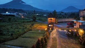 A rural setting with a small, illuminated structure in the foreground, a paved road, and a mountain in the background. - Jawa Dwipa Villa (Wonosobo)