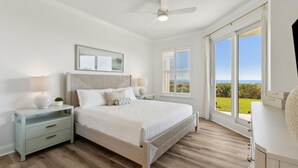 Un dormitorio con cama, mesitas de noche, ventilador de techo y un ventanal con vistas.