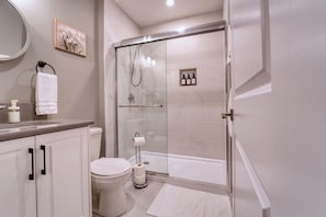 A modern bathroom with a glass-enclosed shower, a toilet, a sink with soap dispensers, and a towel rack.