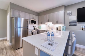 A modern kitchen with stainless steel appliances, grey cabinetry, and a central island with seating.