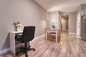 A modern kitchen with a built-in refrigerator, a dining area with a wooden table and chairs, and a workspace with a desk and chair.