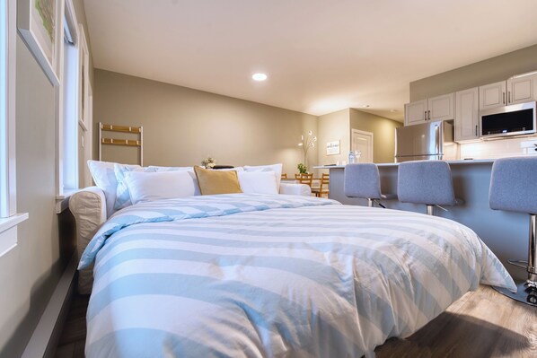 A bedroom with a bed, bedside tables, a desk, and a kitchenette.