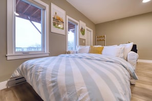A bedroom with a large bed, a window, and artwork on the wall.
