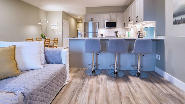 Una cocina moderna con taburetes de bar, un comedor con mesa y sillas, y una sala de estar con sofá.