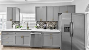 A modern kitchen with grey cabinets, a stainless steel refrigerator, and a patterned backsplash. - 5BR Pool House • Just 15 Min to DFW Airport (Lewisville)