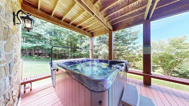 Een hottub onder een houten pergola met stenen muren, omgeven door een terras en een gazon.
