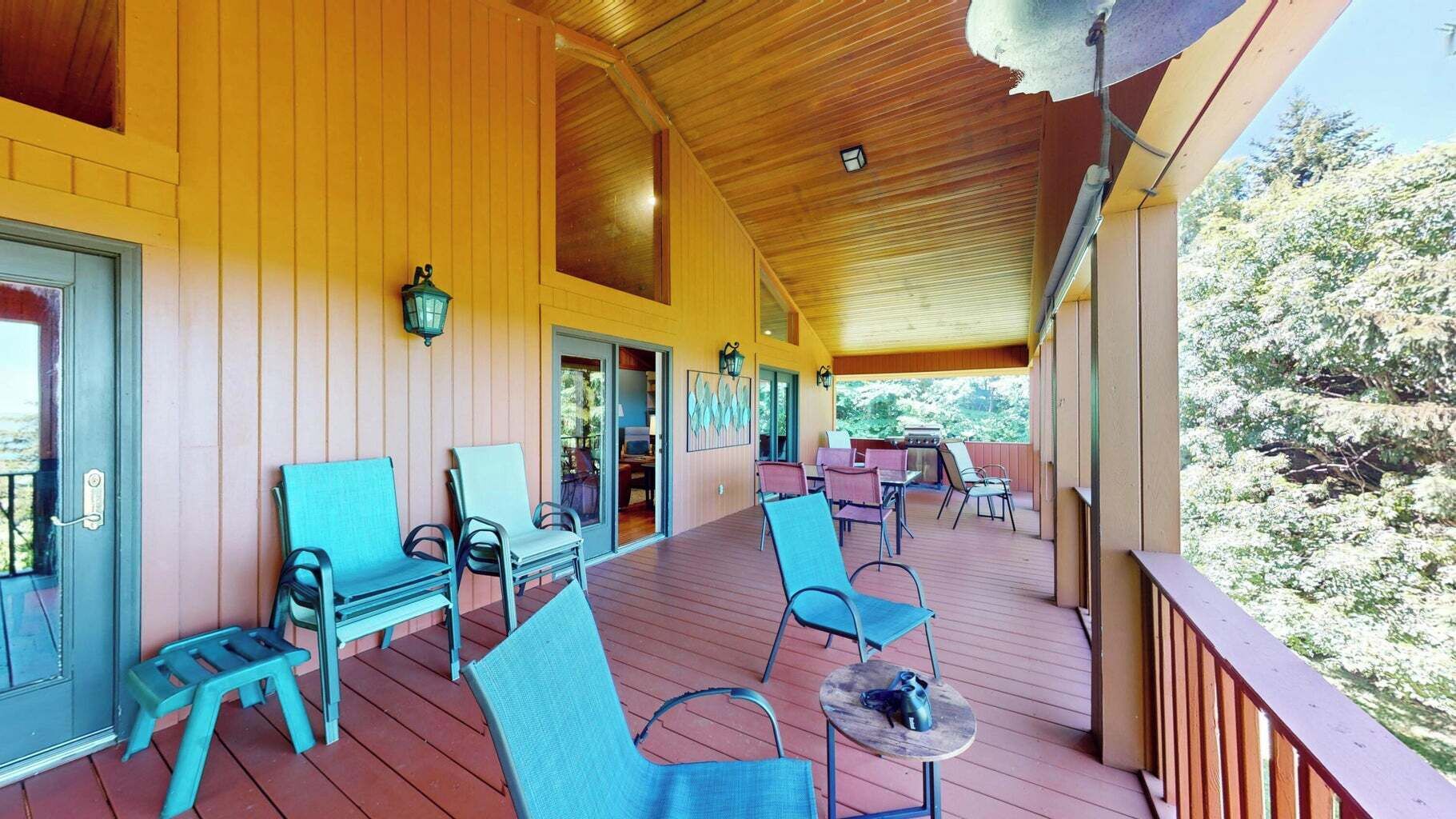 Un espace extérieur abrité, doté de murs et d’un plafond en bois, comprenant plusieurs chaises et tables, et offrant une vue sur un paysage naturel.