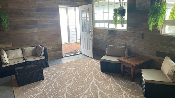A cozy room with wooden walls, a sofa, a chair, a small table, and hanging plants.