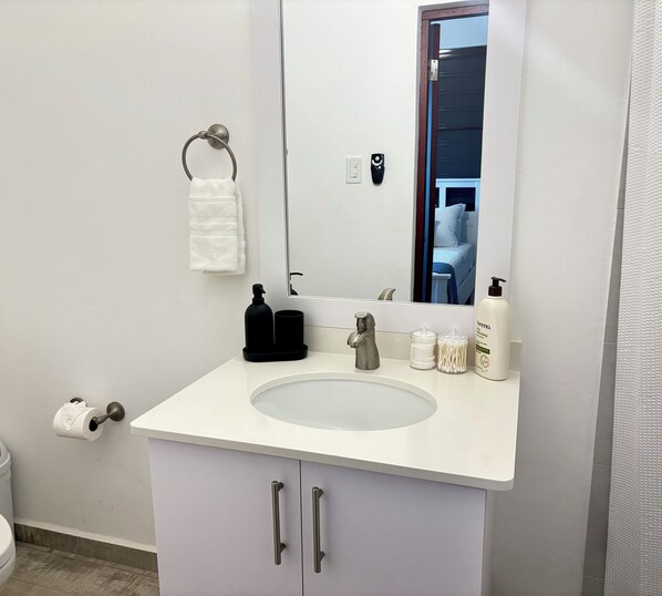 A bathroom with a white sink, a mirror, a towel rack, a toilet paper holder, and a bottle of hand soap.