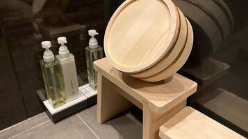 A wooden vanity with a mirror and a wooden stool. There are three bottles of liquid soap on a white stand.