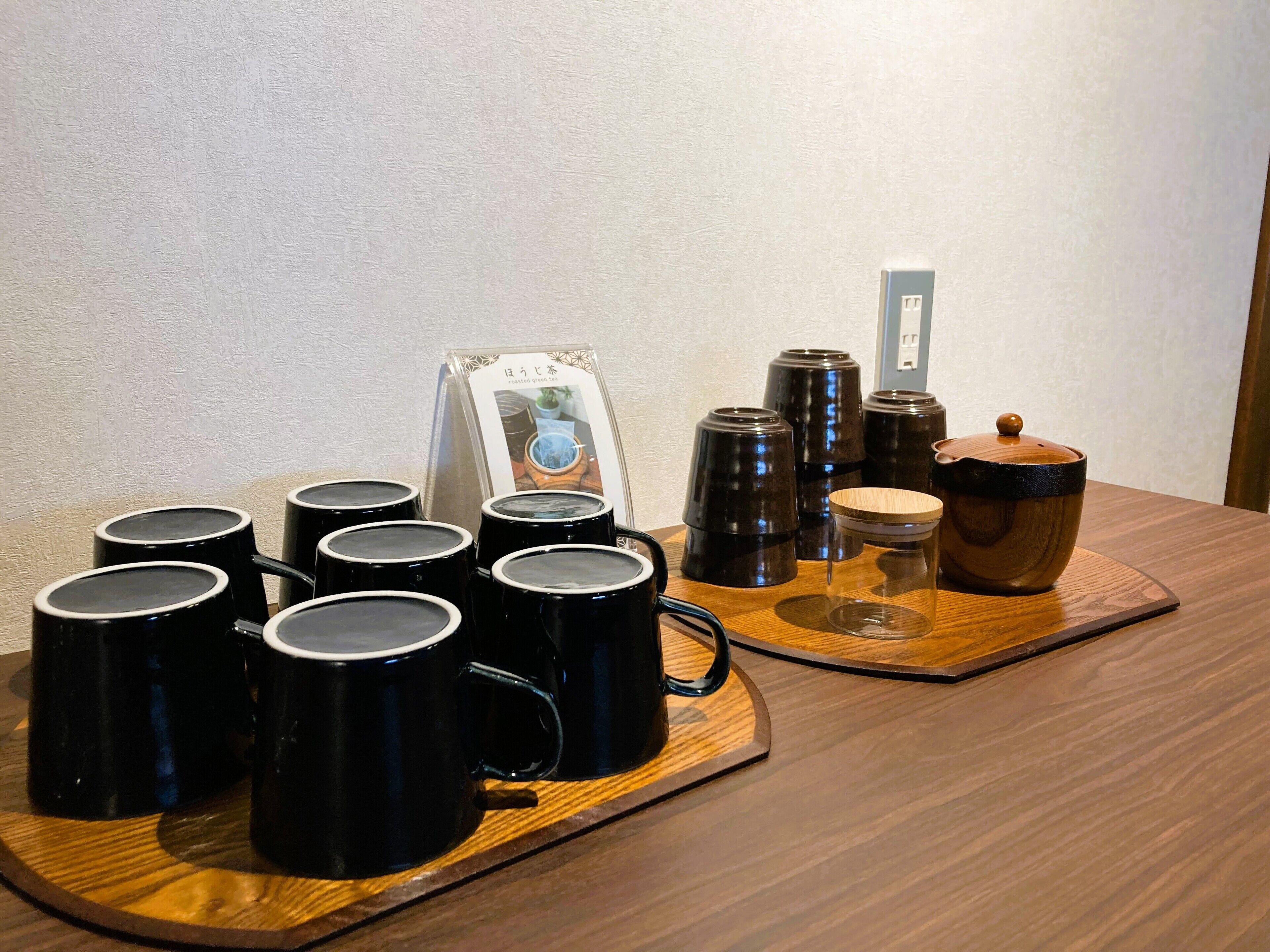 A wooden tray with black mugs, a wooden bowl, and a sign with Japanese text.