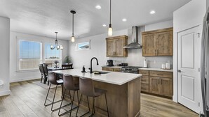 Une cuisine moderne dotée d’un îlot central, de tabourets de bar, de meubles en bois et de luminaires suspendus.