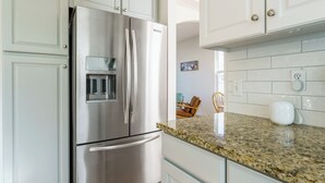 Cucina con mobili bianchi, frigorifero in acciaio inossidabile, piano di lavoro in granito e bollitore elettrico bianco.