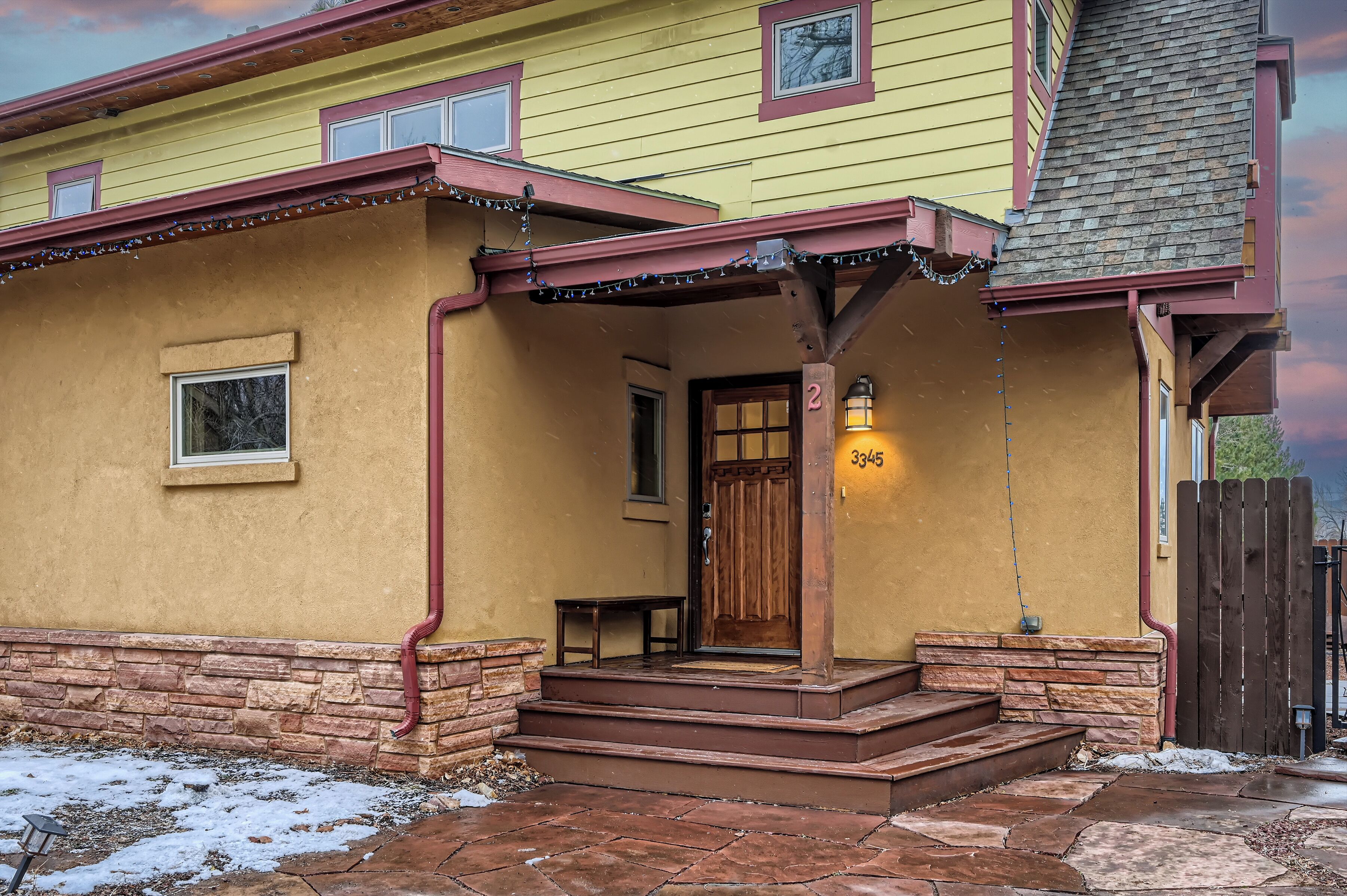 A yellow building with a wooden porch, a door with a number '2' sign, and a stone foundation.