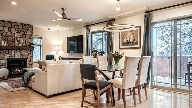 Een ruime woonkamer met een open haard, een eetgedeelte met een glazen tafel en grote ramen met uitzicht op de omgeving.