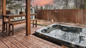 Een houten terras met een jacuzzi, een houten bankje en een tuinhuisje op de achtergrond.
