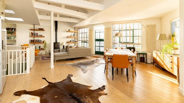 A spacious living area with a high ceiling, wooden flooring, a central seating area, and a dining table.