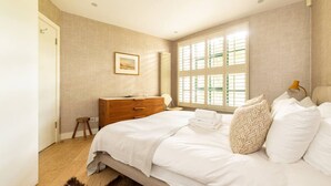A bedroom with a bed, a dresser, a window with blinds, and a framed picture on the wall.