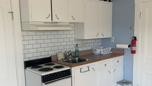 Una cocina compacta con armarios blancos, una estufa y un lavamanos.