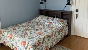 Un dormitorio con colcha estampada de flores, cabecera de madera, dos lámparas de pared y un tapete con diseño.