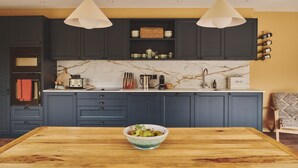 Eine moderne Küche mit dunklen Schränken, einer Marmor-Spritzschutzwand und einem Holzespeisetisch mit Obstschüssel.