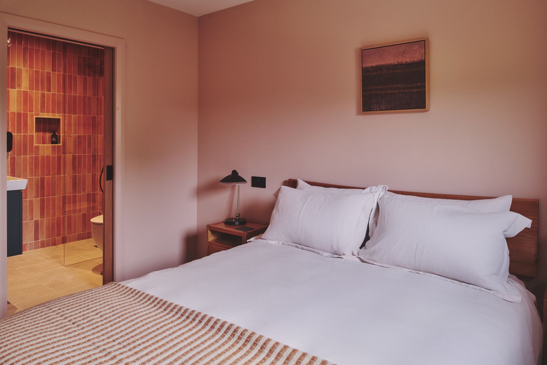 Ein Schlafzimmer mit einem Bett, einem Nachttisch, einer Lampe und einem Gemälde an der Wand.