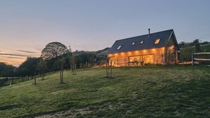 Eine Blockhütte mit geneigtem Dach, einem Schornstein und einer Veranda mit Sitzgelegenheiten.