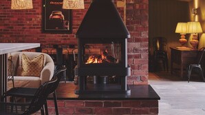 Un intérieur chaleureux avec une cheminée en briques, des poutres en bois et des luminaires suspendus.