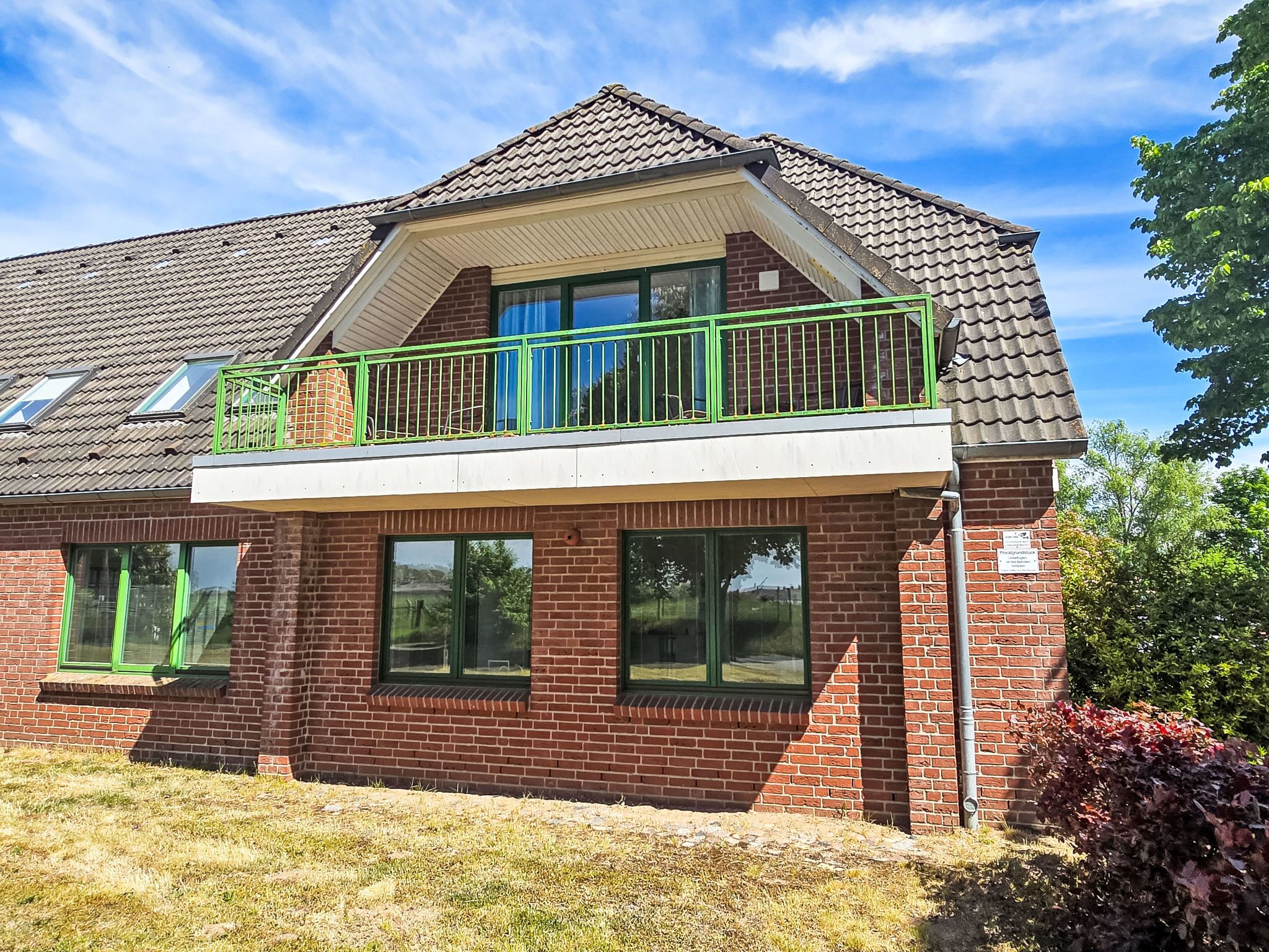 A two-story house with a balcony, large windows, and a brick exterior.