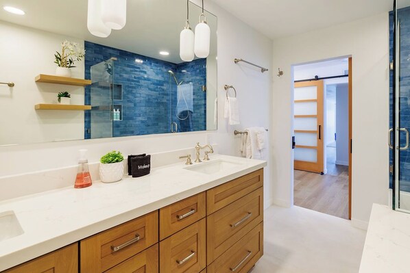 A modern bathroom with a large mirror, a white sink, wooden cabinets, and a blue-tiled shower area.
