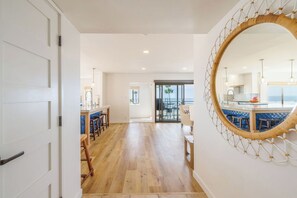 Un intérieur spacieux avec un plancher en bois, un coin repas doté de tabourets de bar bleus et un grand miroir orné d’un cadre décoratif.