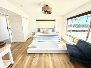 Ein Schlafzimmer mit einem großen Bett, einem Fenster mit Aussicht, einer Lampenschirm aus Weidengeflecht und einem Sessel.