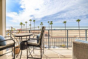 A balcony with wicker furniture, a view of the beach, and palm trees.