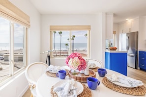 A dining area with a view of the beach, a kitchen with blue cabinets, and a large window with a view of palm trees.