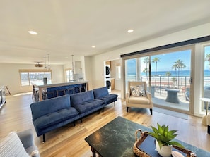 A modern living room with a blue sofa, a dining area, and a view of the beach.